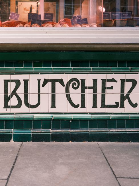 The exterior of a shop called 'The Garden Shop' features large glass windows revealing a variety of garden-related items and decorations inside, including potted plants, gardening ornaments, and flora